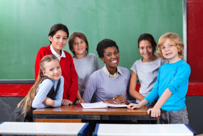 Portrait of happy African American female teacher and schoolchildren together at desk in classroom
